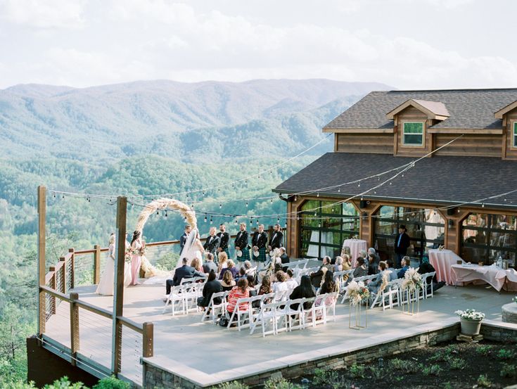 a group of people sitting on top of a wooden platform next to a building with mountains in the background