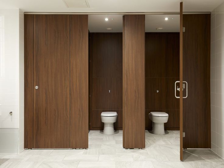 two toilets in a bathroom with wooden partitions and white tile flooring on the walls