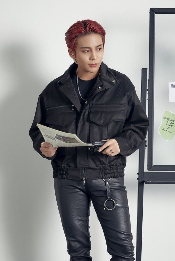 a young man with red hair is standing in front of a whiteboard and holding a piece of paper