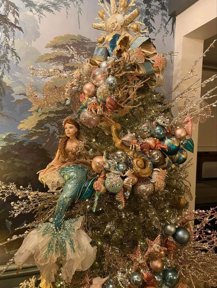 a christmas tree decorated with mermaids and ornaments in gold, silver and blue colors