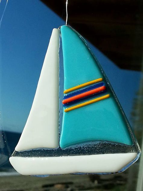 a sailboat ornament hanging from the side of a window with blue sky in the background