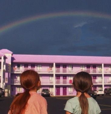 two girls standing in front of a motel with a rainbow in the sky above them