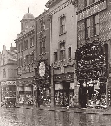 an old black and white photo of people walking down the street in front of stores