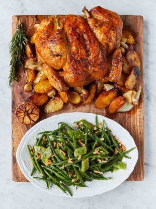 roasted chicken and green beans on a wooden cutting board with rosemary garnishes