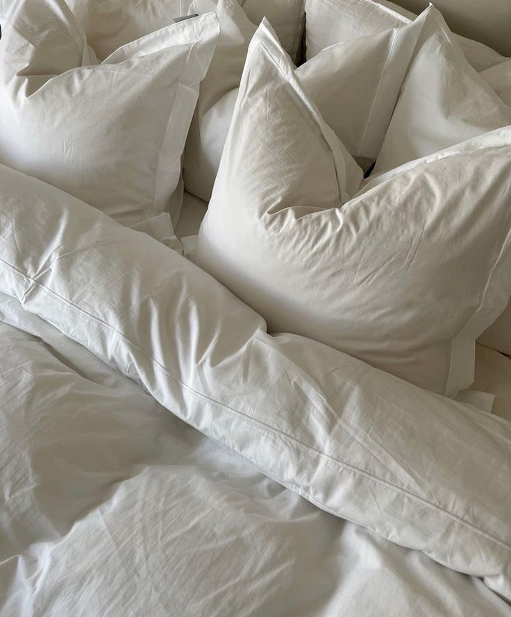 an unmade bed with white sheets and pillows