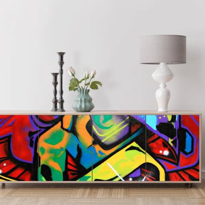 a sideboard with colorful graffiti painted on it in a living room next to a lamp