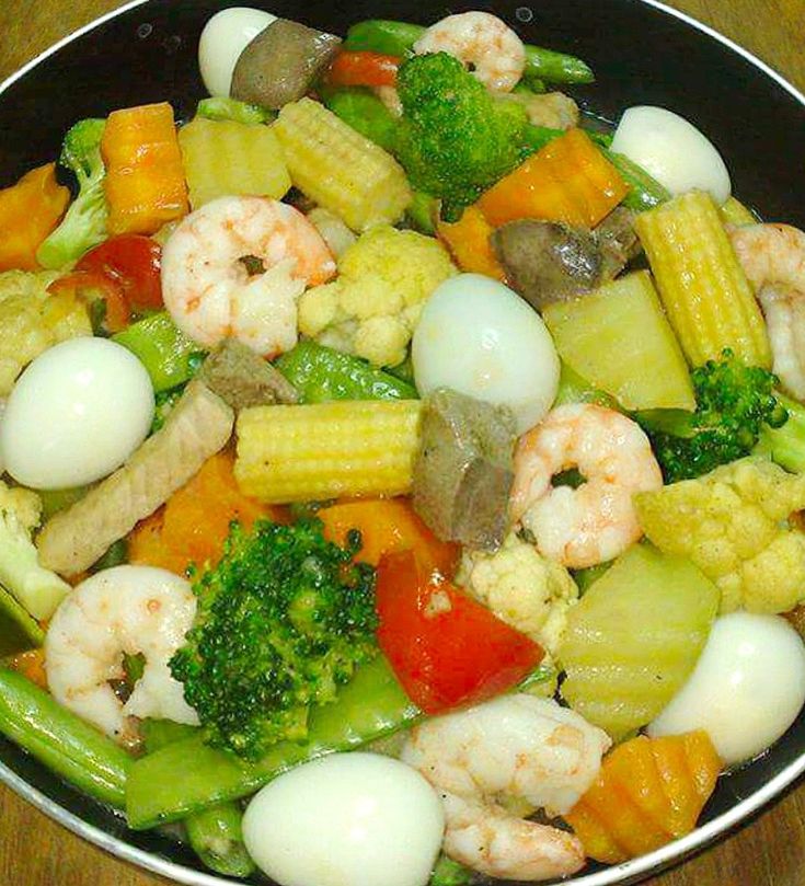 a pan filled with vegetables and shrimp on top of a wooden table