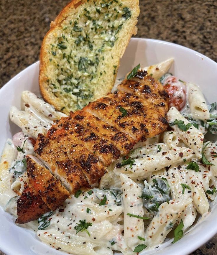 a white bowl filled with pasta and meat next to a piece of bread on top of a table