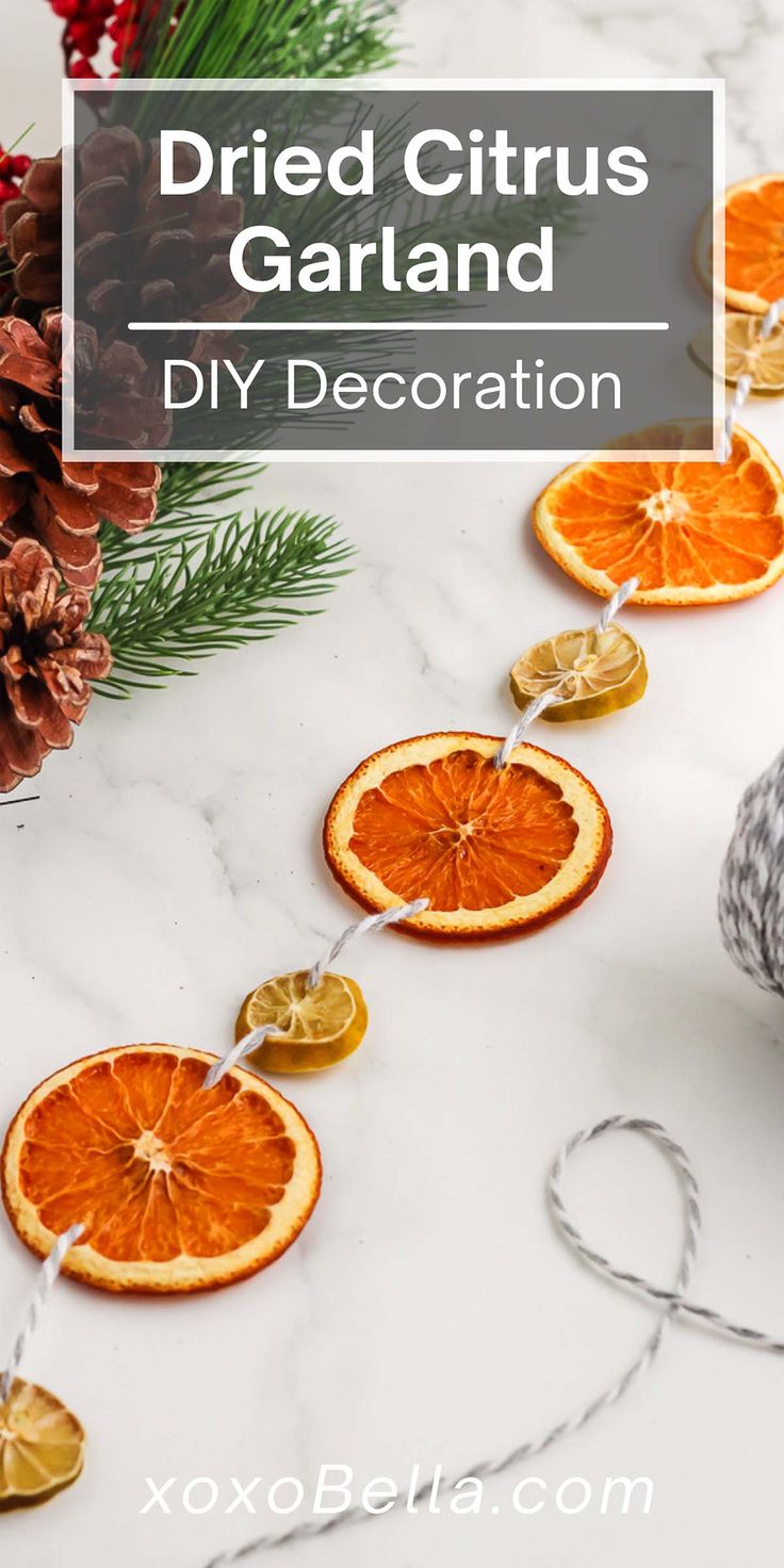 dried citrus garland with orange slices and pine cones on white marble countertop next to christmas decorations