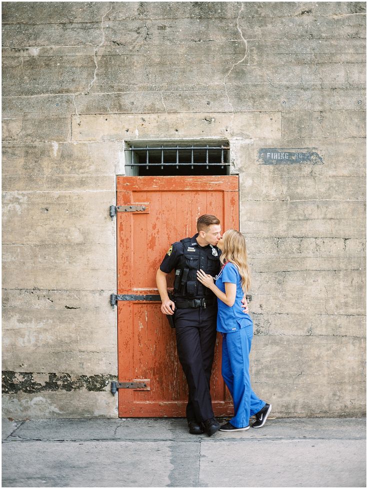 a police officer standing next to a woman in front of a red door and holding her head against the wall