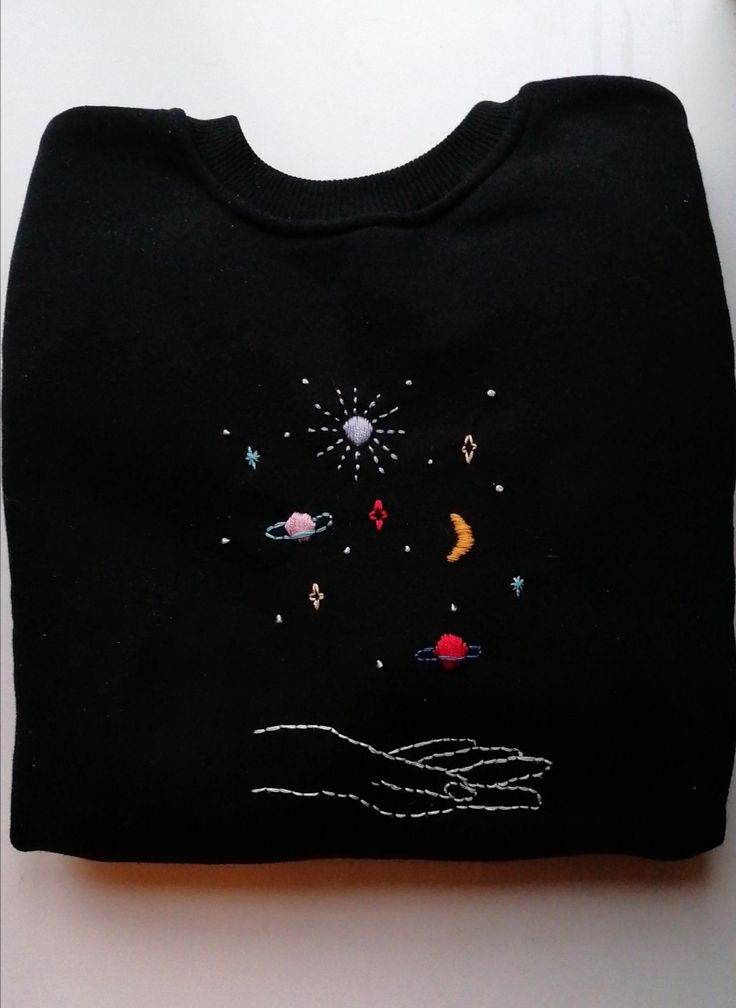 a black t - shirt with an embroidered space scene on the front and hand holding it