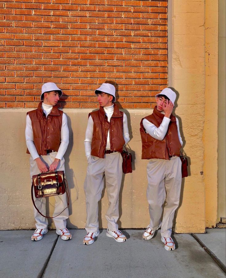 three men in brown vests and white hats are standing next to a brick wall