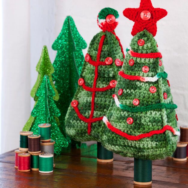 three crocheted christmas trees sitting next to each other on top of a wooden table