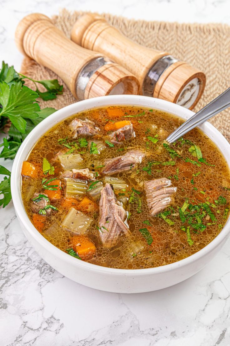 a bowl of soup with meat, carrots and parsley next to it on a table