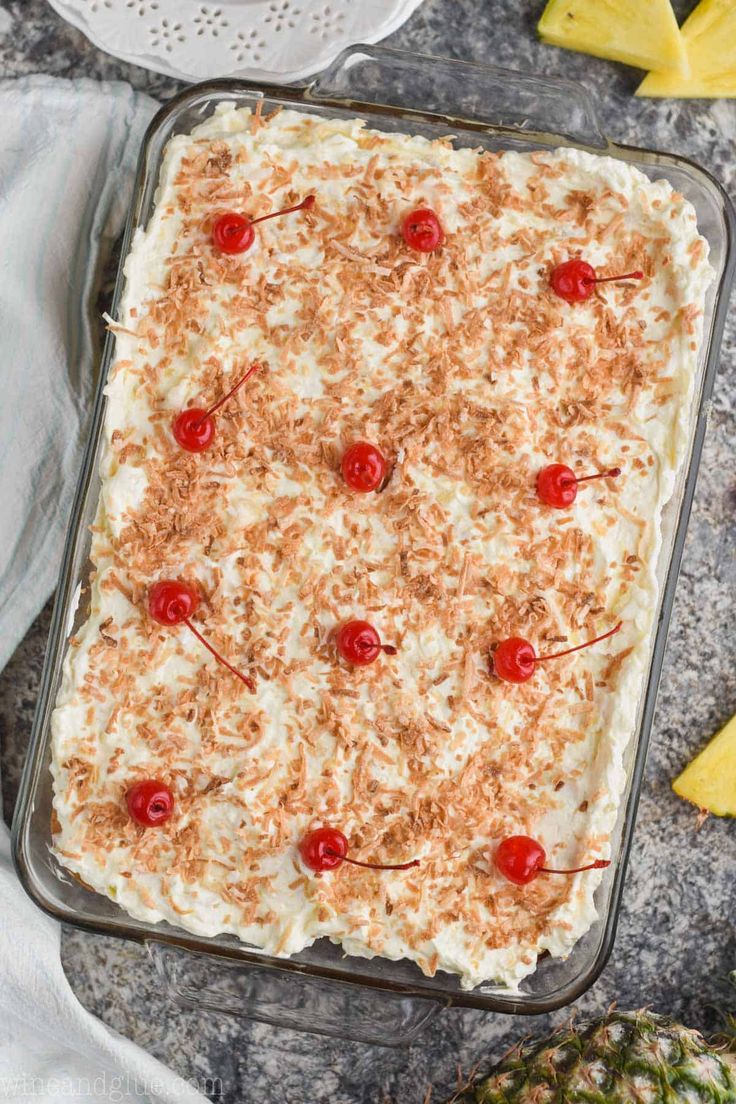 a pineapple dessert in a glass baking dish with cherries on the top and two slices of pineapple next to it