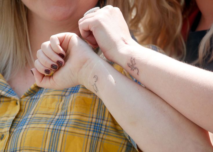 a woman with two tattoos on her arm holding onto another person's hand and smiling at the camera