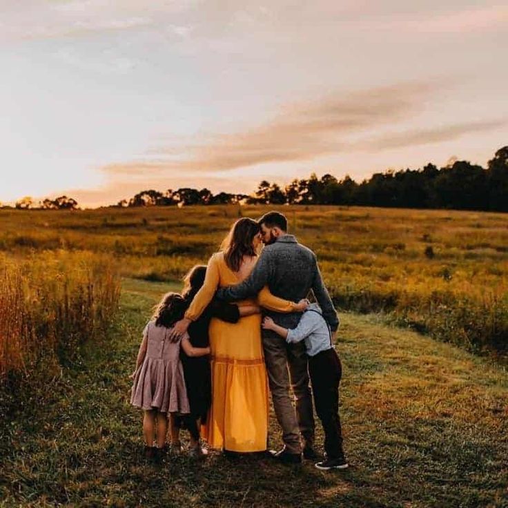 a family hugging each other in the middle of a field at sunset with trees and grass behind them