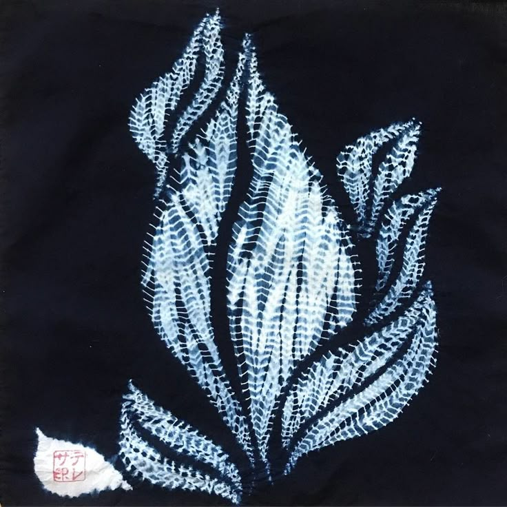 an embroidered piece of cloth with blue and white designs on it, in the shape of a leaf