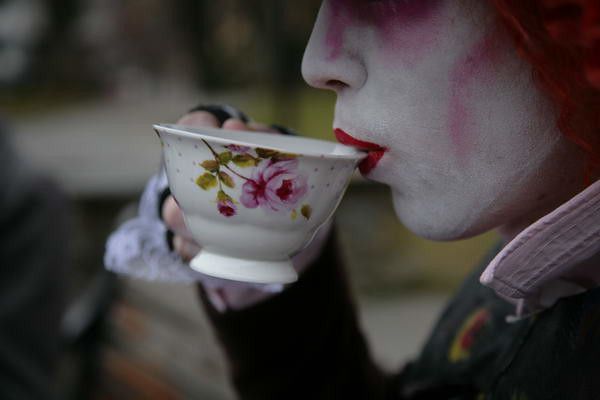 a woman with painted face drinking out of a tea cup in front of her face