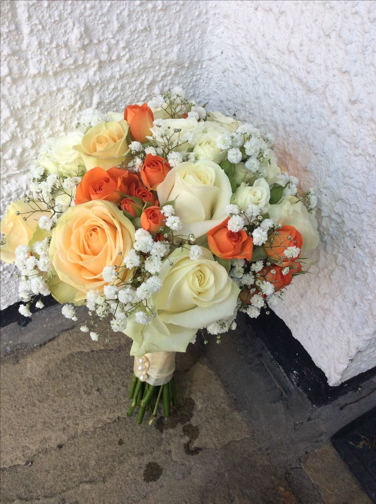 a bridal bouquet with orange and white flowers on the ground next to a wall