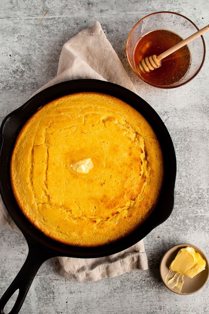 a cast iron skillet filled with cornbread next to a cup of honey and spoon