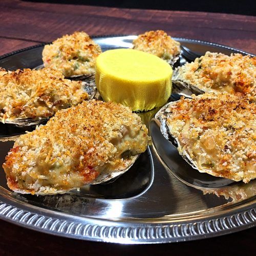 several oysters on a silver plate with a yellow sauce in the middle and a glass of water next to it