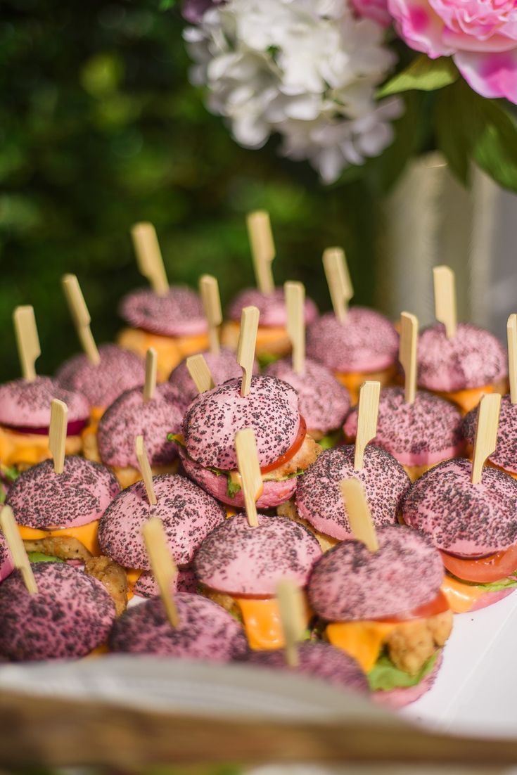 there are many mini sandwiches with toothpicks in them on the table next to flowers