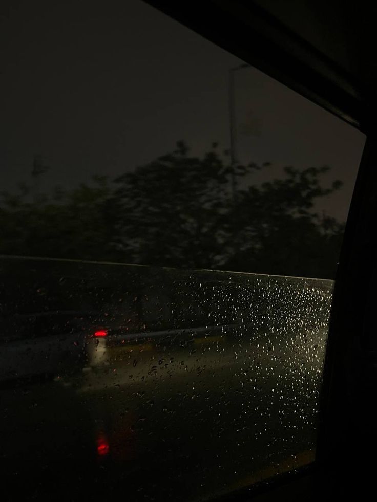 rain drops on the windshield of a car as it drives down a road at night