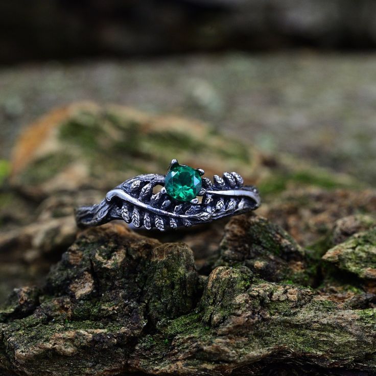 a ring with an emerald stone in the middle on top of some mossy rocks