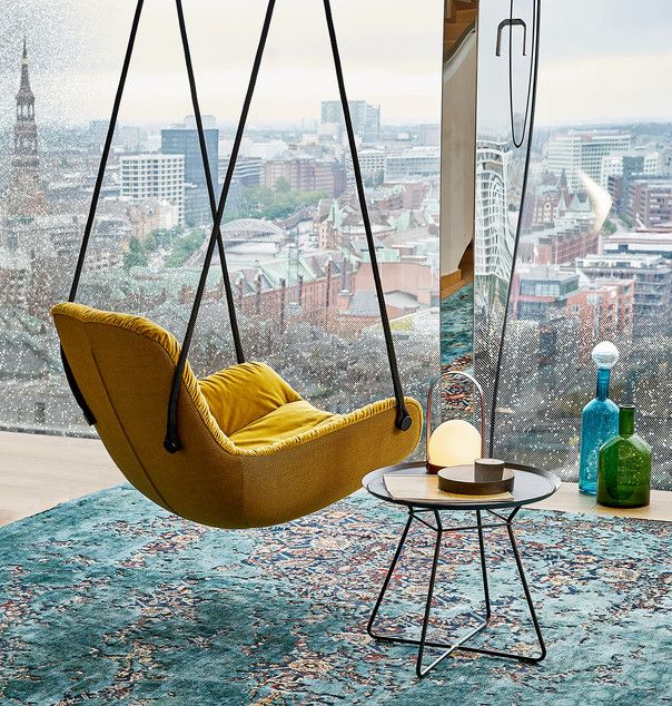 a hanging chair in front of a window with cityscape behind it and a table on the other side