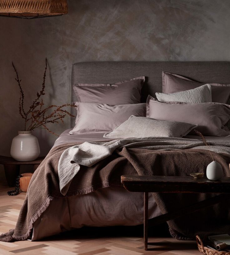 a bed with pillows and blankets on top of it next to a table in front of a wall