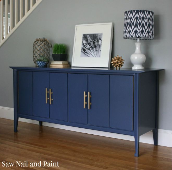 a blue sideboard with two pictures on top and a lamp next to it in front of a stair case