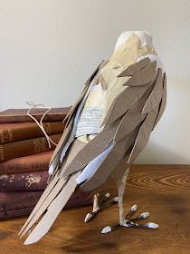 a bird made out of paper sitting on top of a wooden table next to books