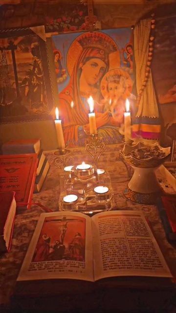 candles are lit in front of an open book with pictures on the wall behind it