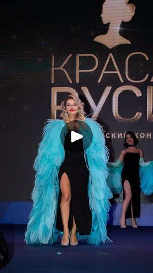 a woman in a black dress and blue feathered coat on the catwalk at an event