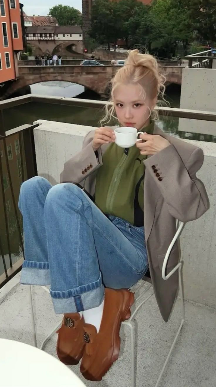 a woman sitting on a ledge drinking from a cup