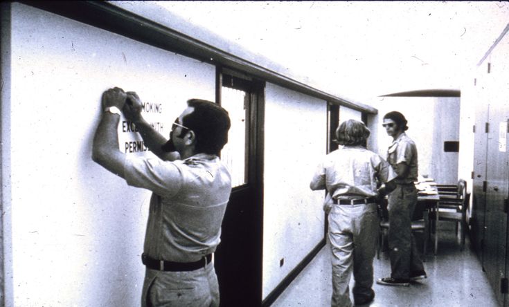 three men are standing in a hallway and one is writing on the wall with marker