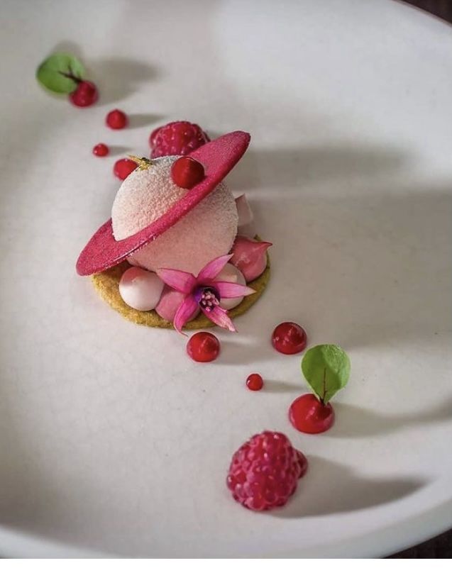 a white plate topped with a dessert covered in icing and raspberry toppings