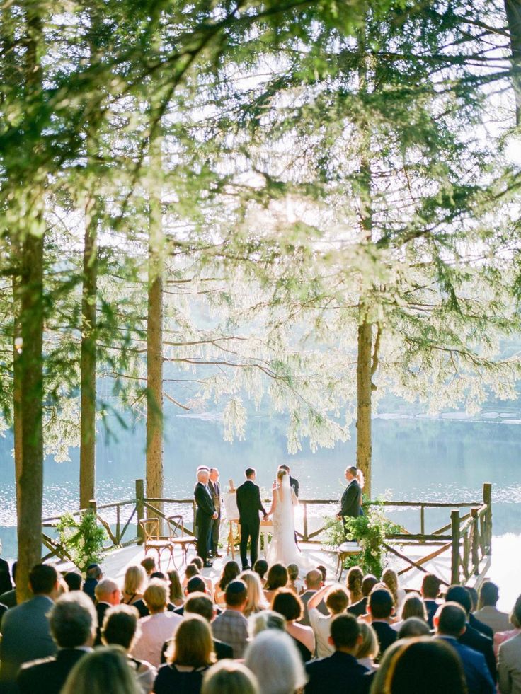 a wedding ceremony on the deck of a lake with people standing in front of it