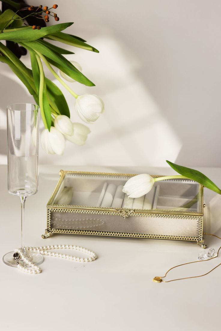 a vase filled with white flowers next to a box and two glasses on a table