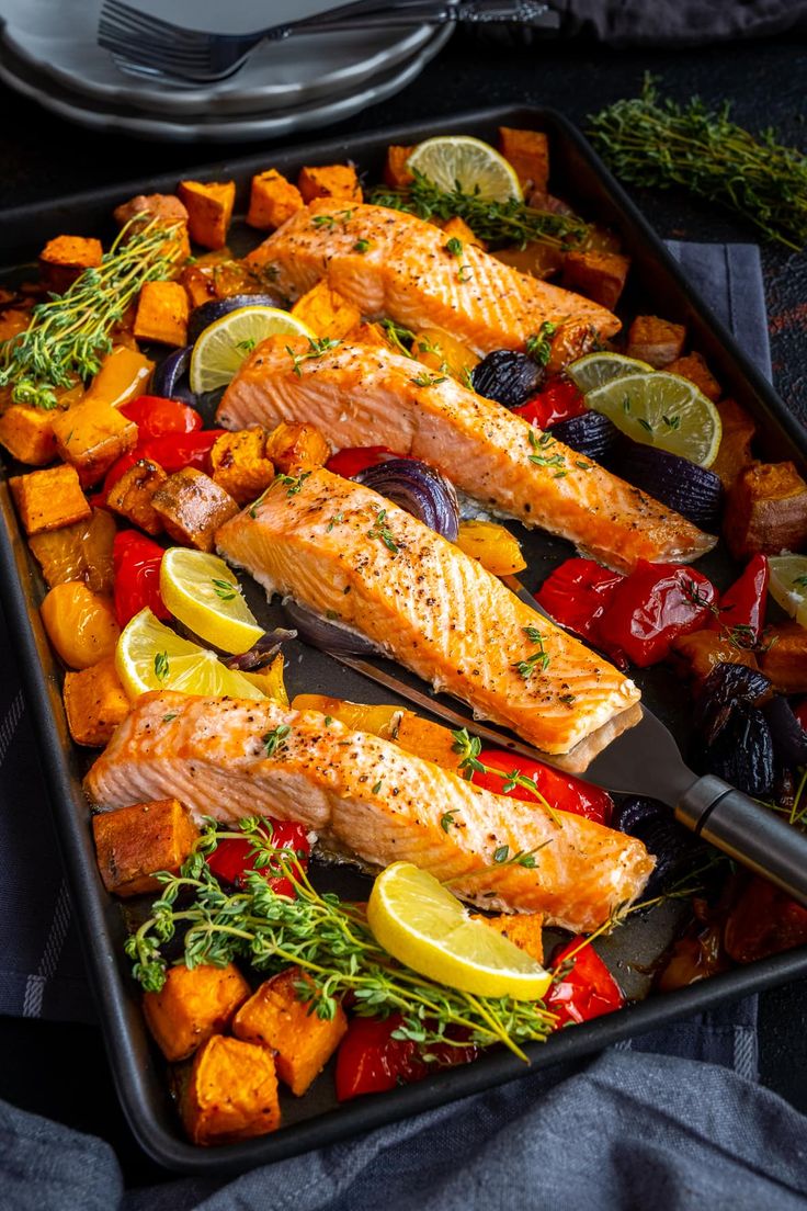 a pan filled with salmon and vegetables on top of a table