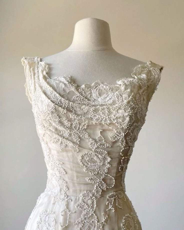 a white wedding dress on a mannequin with beading and flowers in the back