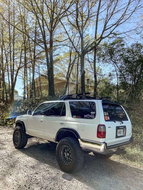 a white truck parked on the side of a dirt road in front of some trees