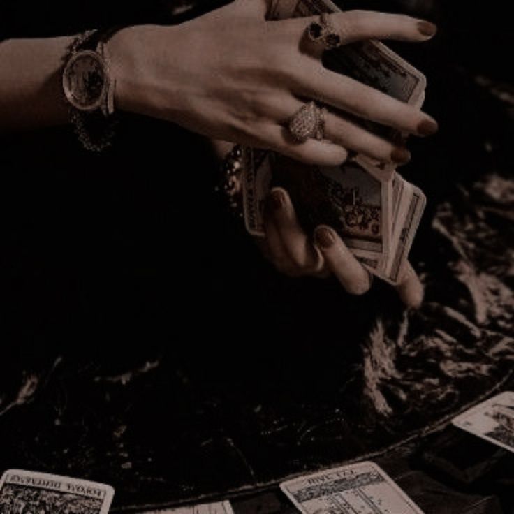 a woman's hands holding playing cards on top of a table