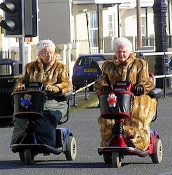 two elderly people riding scooters down the street