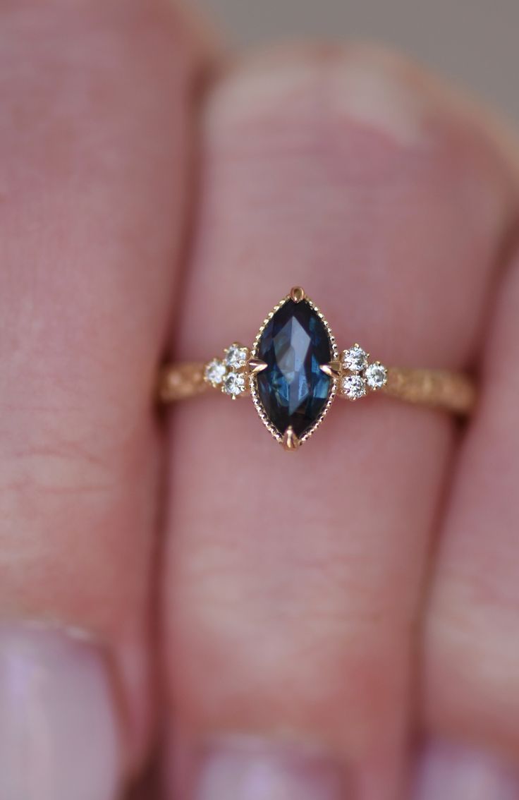 a woman's hand holding a ring with a blue stone and three diamonds on it