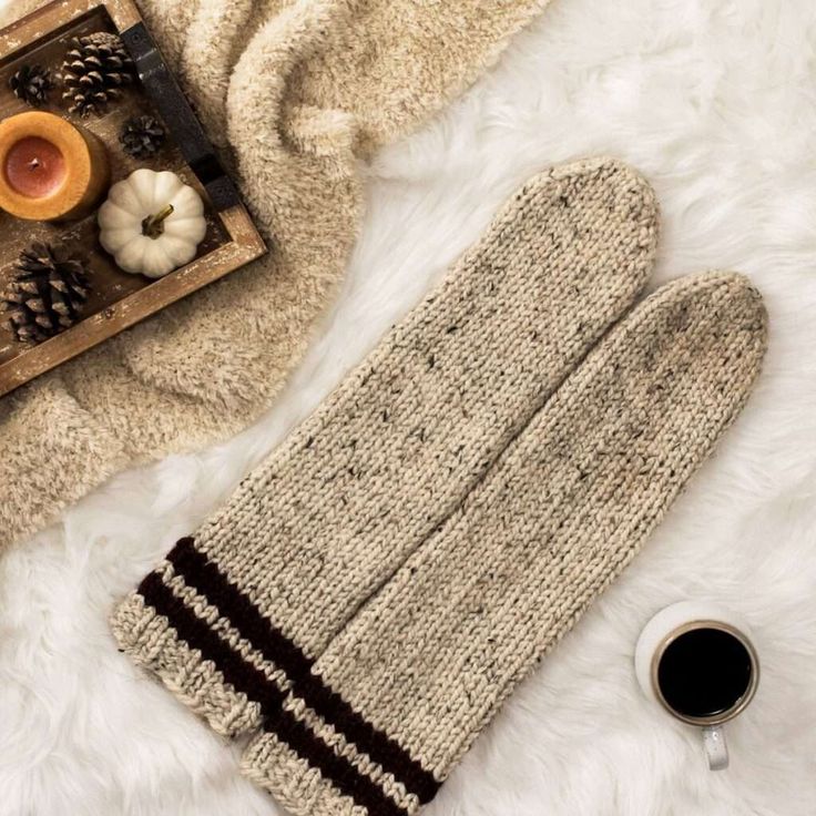 a pair of knit mittens next to a cup of coffee on a white fur rug