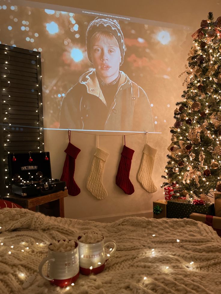 a christmas tree with stockings hanging from it and two mugs on the bed next to it