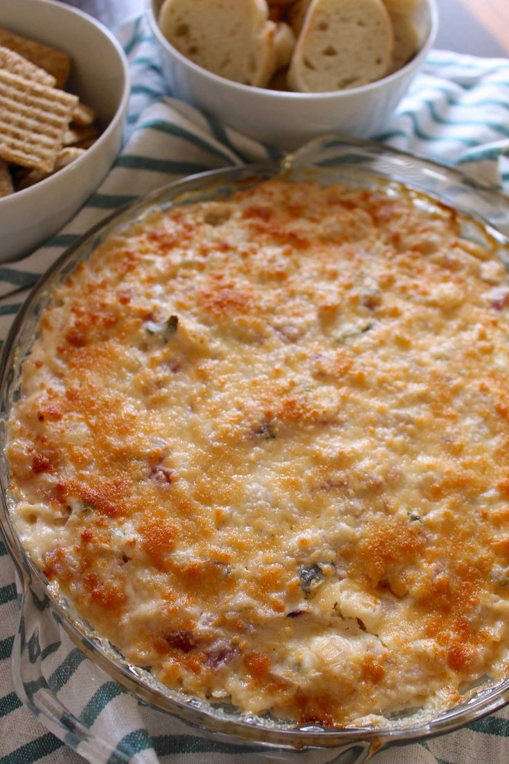 a casserole dish with cheese and crackers in bowls on a tablecloth