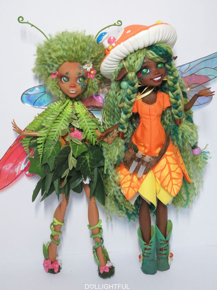 two dolls are dressed in green and orange fairy costumes, one is holding a plant